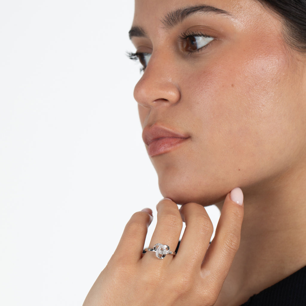 Close-up of a woman wearing a diamond  and sterling silver love knot ring on a plain background